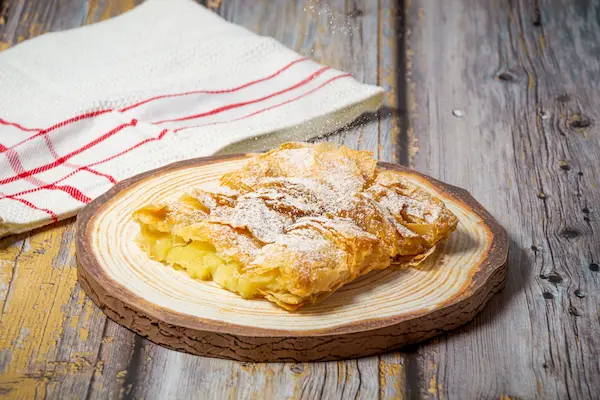 Bougatsa tradiționala greceasca cu foietaj si zahar pudra pe platou de lemn, Salonic, Grecia